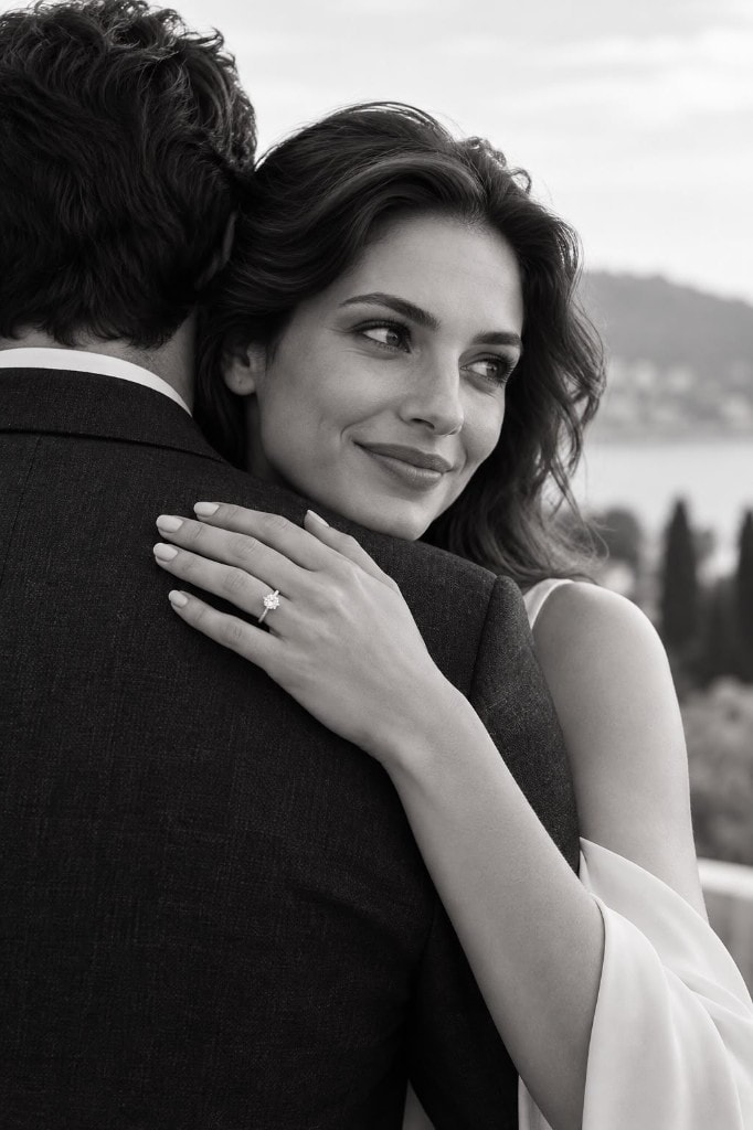 Couple embracing by the coast, a diamond ring catching the light on her hand