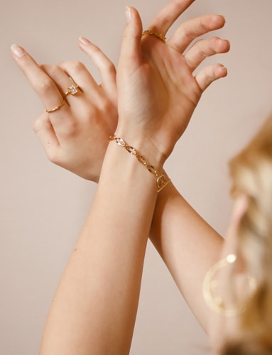 Hands wearing stacked Vallière gold chain bracelets and rings